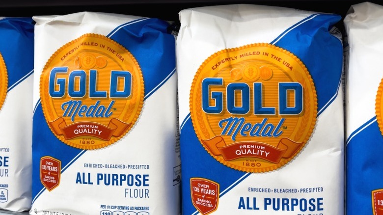 Bags of Gold Medal All Purpose Flour on a supermarket shelf.