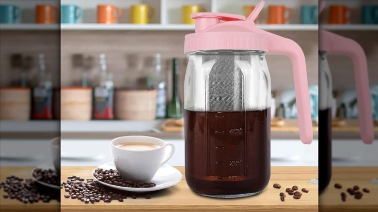 pink QHH cold brew coffee maker on a kitchen counter next to a cup of coffee and a pile of coffee beans