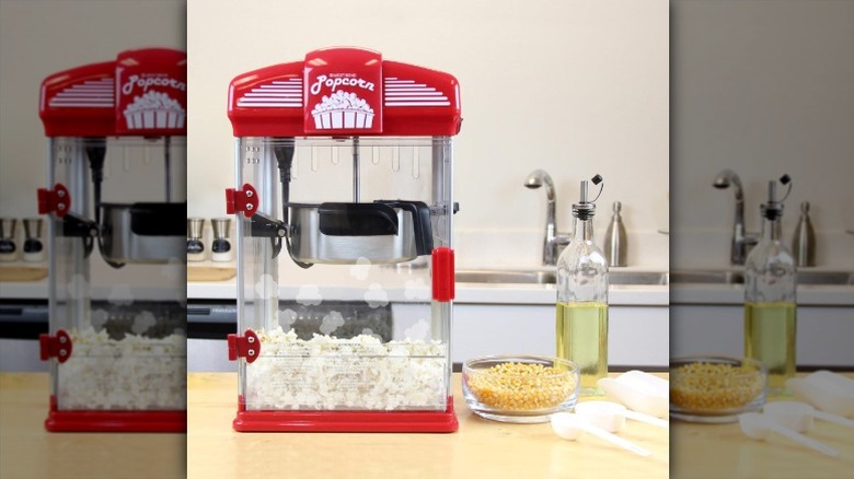 red West Bend Stir Crazy popcorn maker on a kitchen counter next to a bowl of popcorn kernels and a bottle of oil
