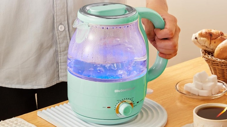 hand holding the handle of a mint green Elite Gourmet electric tea kettle