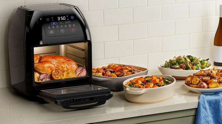 whole chicken and red onions in a Chefman air fryer on a kitchen counter next to several dishes filled with cooked vegetables