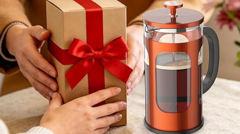 hands holding a gift box with a red ribbon next to a copper-colored Veken French press