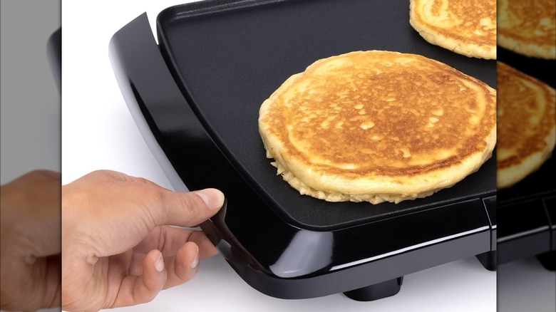 Hand touching bottom of Presto Cool Touch electric griddle cooking pancakes