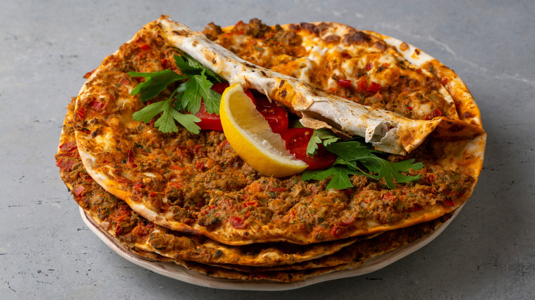 a stack of lahmacun, flatbread baked with spices, topped with lemon wedge, tomato chunks, and flat-leaf parsley