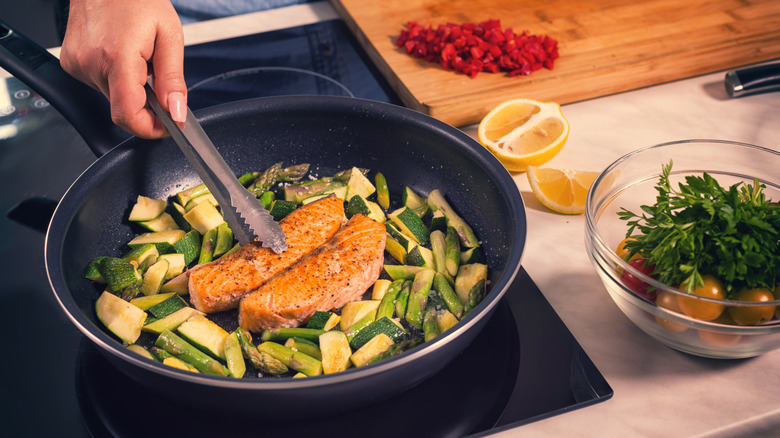 woman searing salmon and veggies in a skillet