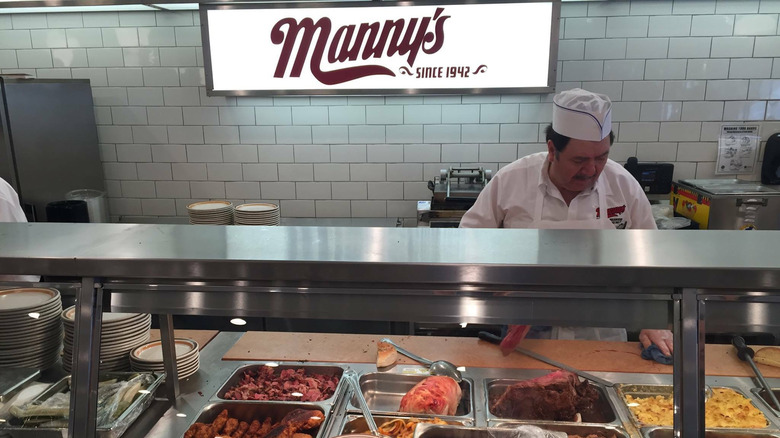 Man prepares food behind sneeze guard at Manny's cafeteria