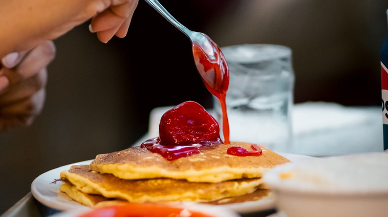 Hand uses spoon to drizzle berries over pancakes