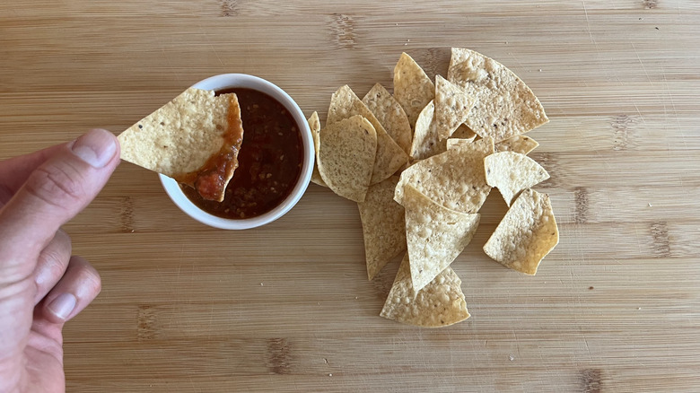 A hand dipping a chip in salsa