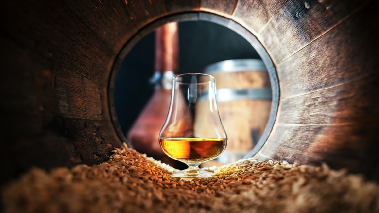 Glass of bourbon inside a barrel with still in the background
