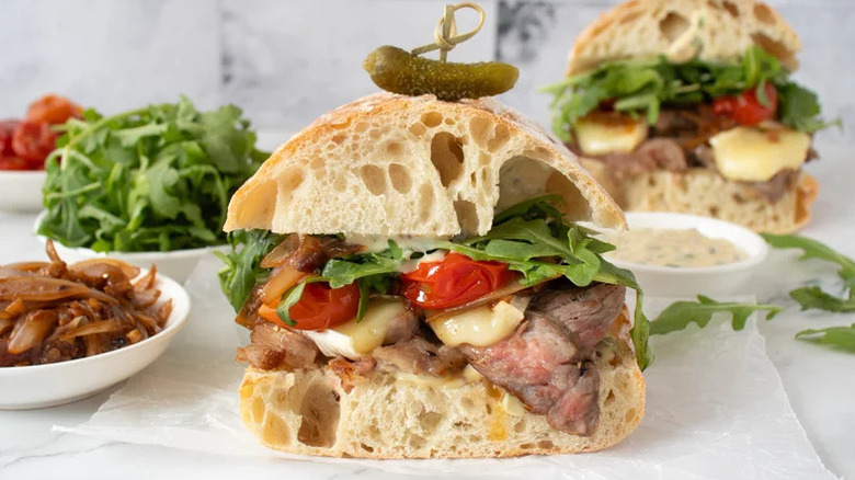 Garlic butter steak sandwich, cut in half, with ingredients in the background