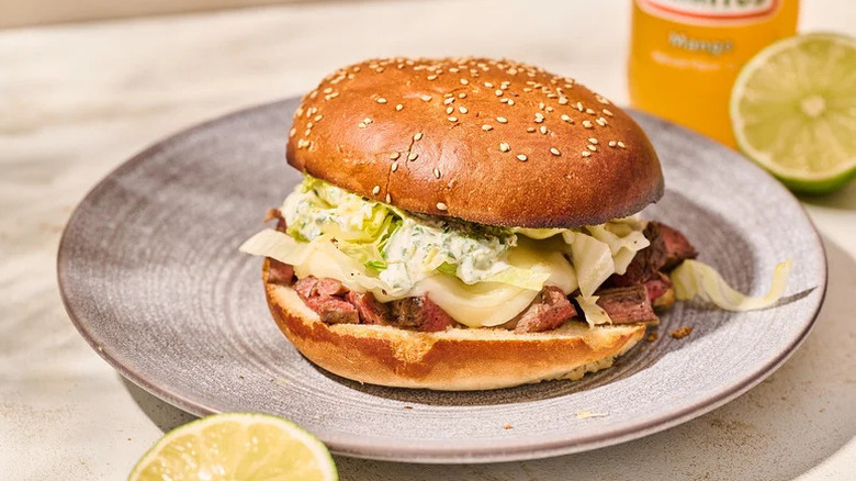 Mexican steak and cheese torta on a platter next to a lime and Jarritos