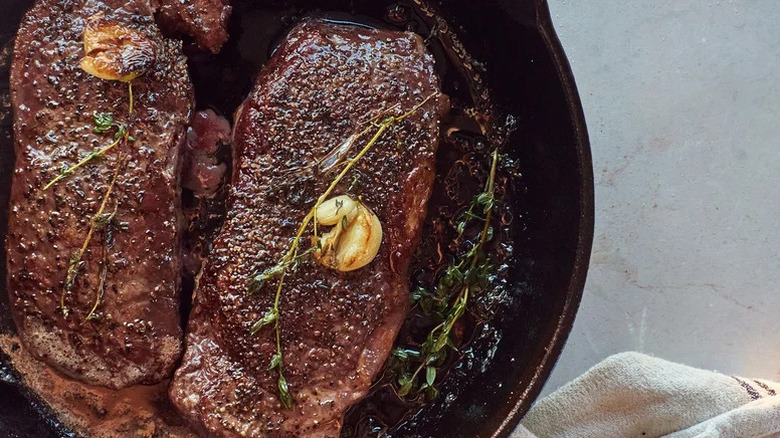 Seared steaks in a cast-iron pan with butter and garnish