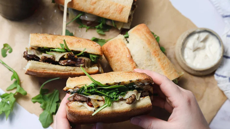 Hand holding a piece of a ribeye steak sandwich with aioli on the side