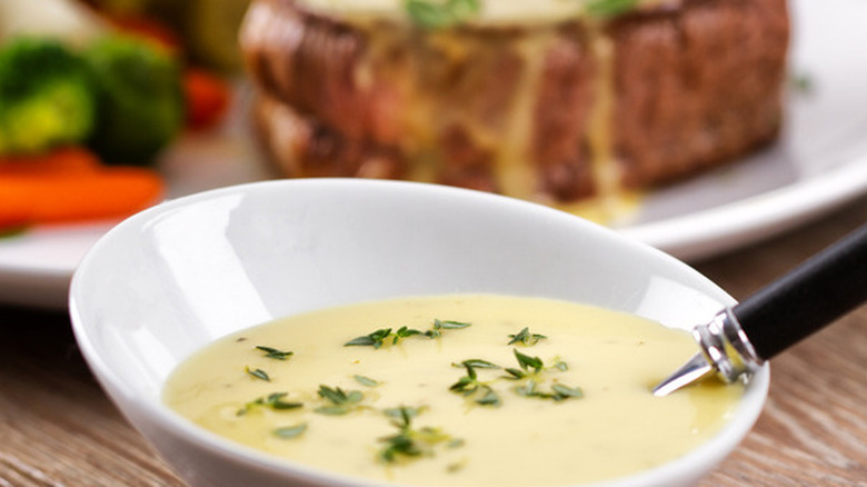 Béarnaise sauce in a bowl, with steak and vegetables in the background