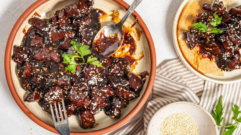 Sticky soy steak bites on a plate with a bowl of sesame seeds on the side