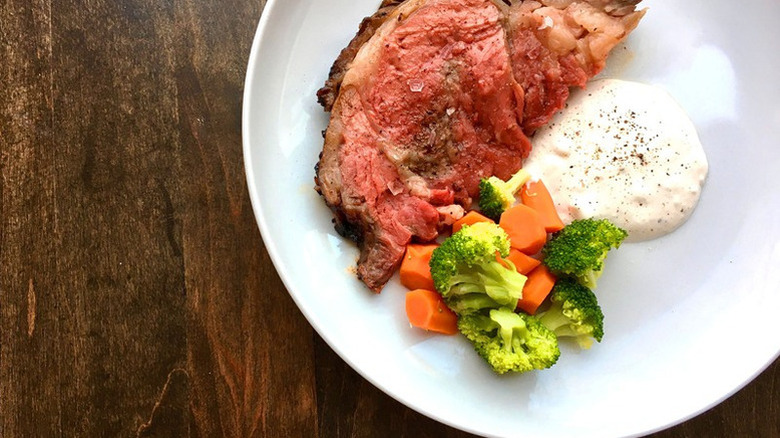 A plated beef rib roast with sauce and vegetables on the side
