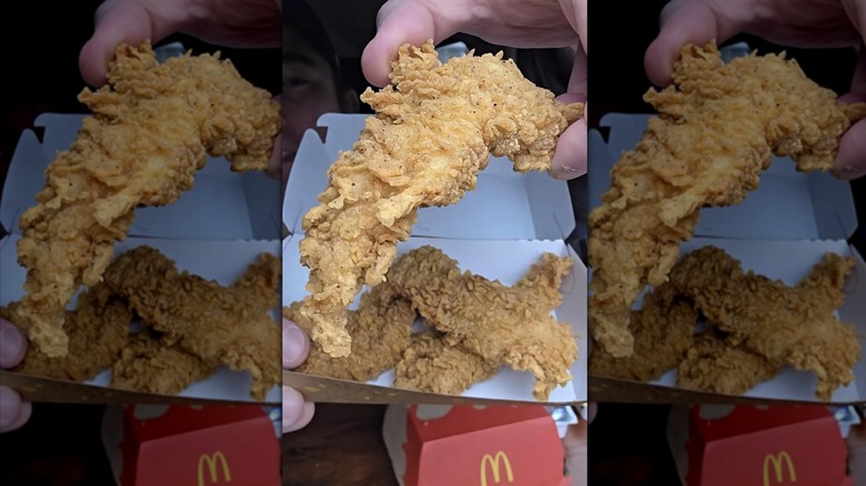 Someone holding a McCrispy strip above a container with more strips.