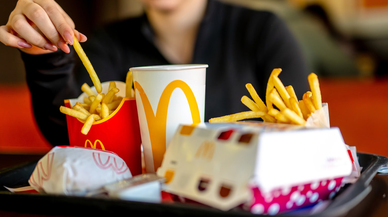 A woman with pink nails sitting inside a McDonald's with a full tray of food in front of her.