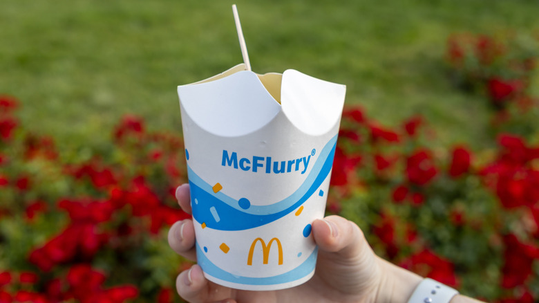 A hand holding a McFlurry and spoon outside.