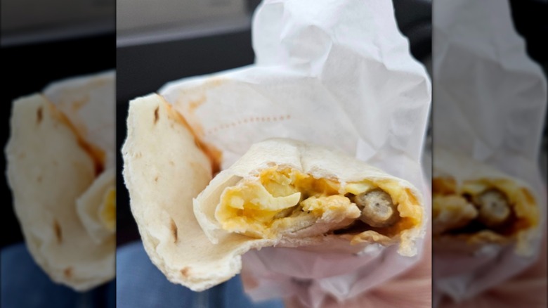 A hand holding a partially consumed sausage burrito.