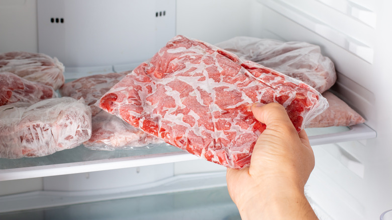 hand takes frozen meat package out of freezer