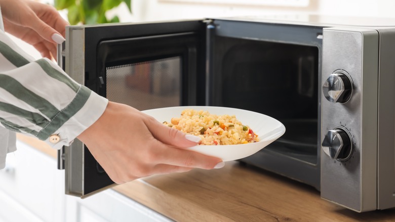woman puts rice dish in microwave oven