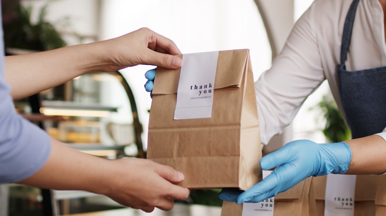 cashier hands paper bag with thank you note to customer