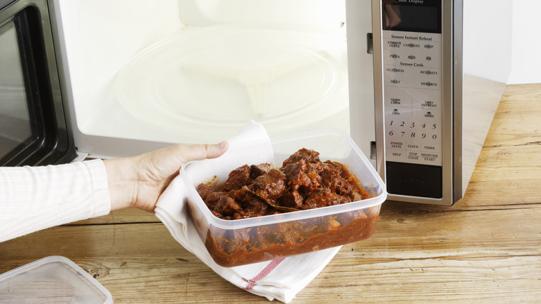 hand puts plastic container filled with beef dish in microwave