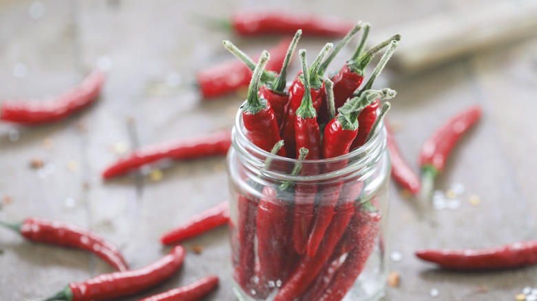 glass jar with spicy peppers by loose peppers