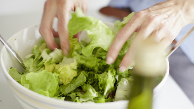 Hands tossing lettuce is a bowl