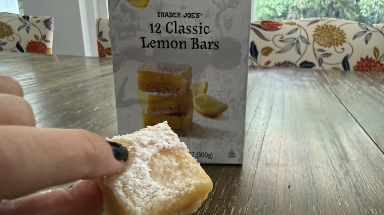 Trader Joe's Classic Lemon Bars package on wooden table and a hand holding a lemon bar