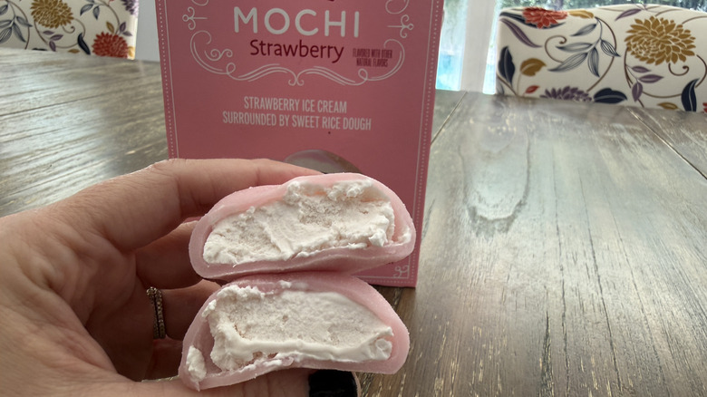 Trader Joe's Strawberry Mochi package on wooden table and a hand holding a mochi split in half