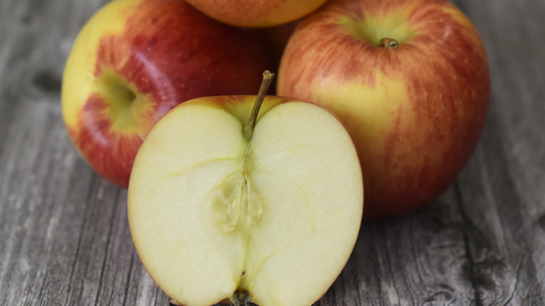 Braeburn apples on a wood table with one apple cut in half to show white flesh