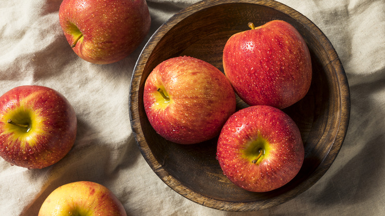 Envy apples in a wooden bowl on tan cloth