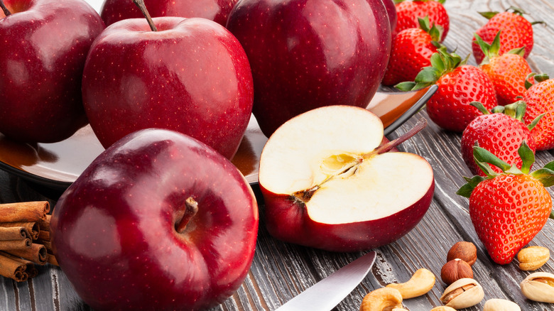 Red Delicious apples on wooden surface with strawberries, cinnamon, and nuts