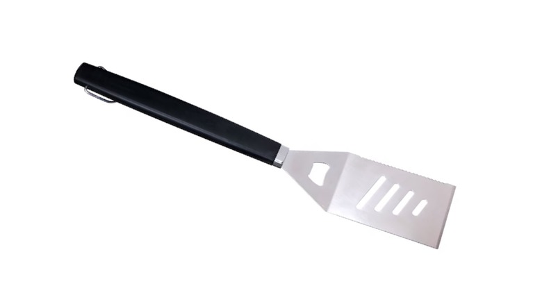 A black and stainless steel spatula with a bottle opener close to the handle on a white background.