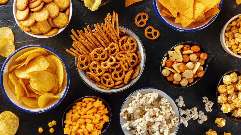 A table of snacks such as popcorn, pretzels, and chips in bowls shot from above