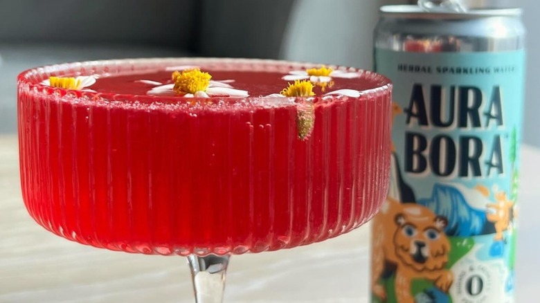 Aura Bora can next to a pink drink in a stemmed glass