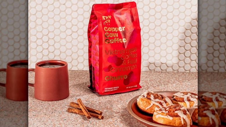bag of Copper Cow churro-flavored coffee with a cup of coffee and plate of cinnamon rolls