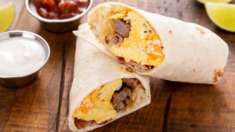 Breakfast burrito cut in half on a table with white and red sauces