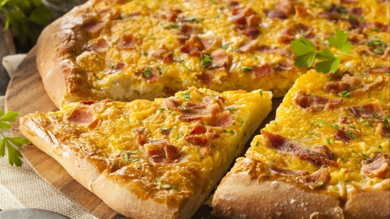 A breakfast pizza topped with eggs, bacon, and cheese with a slice cut out