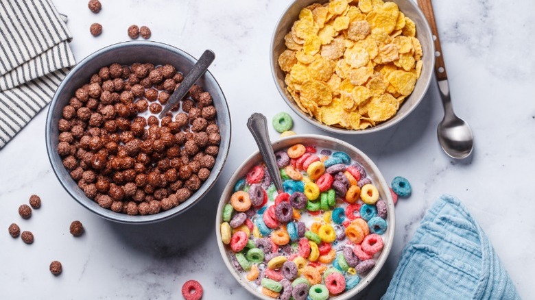 Three bowls of cereal on a marble counter with cocoa puffs, fruit loops, and frosted flakes