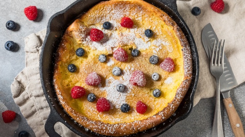 Dutch baby in a cast iron skillet topped with powdered sugar and berries