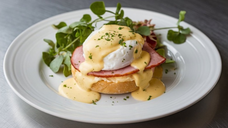 Eggs benedict with poached egg, canadian ham, hollandaise, and garnish on an english muffin