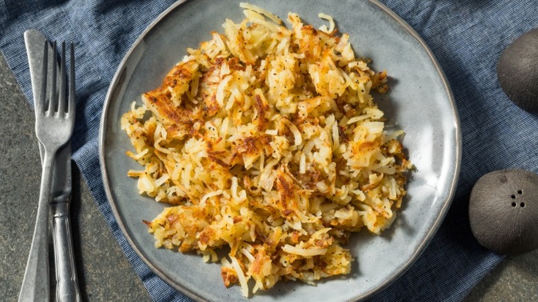A plate of golden brown hash browns with silverware and saltshakers