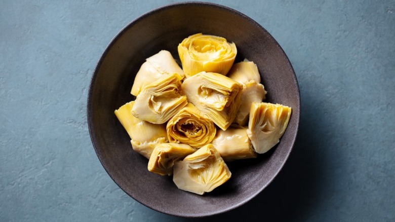An overhead shot of a black plate of artichokes on a blue countertop