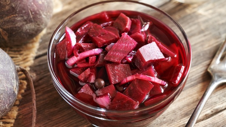 A glass bowl filled with sliced beets on a wooden counter