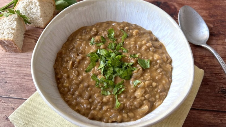 A bowl of lentils with a green garnish and silverware on a wooden table