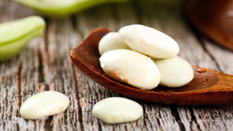 A close-up of a wooden spoon holding white lima beans on a wooden surface