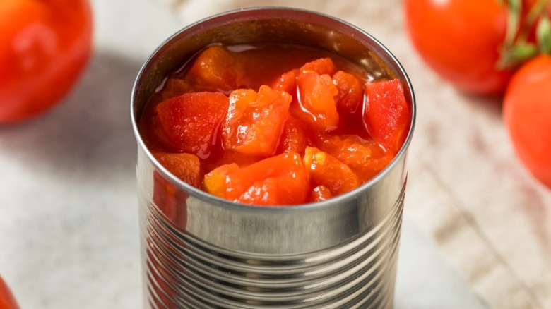 An open can of diced tomatoes on a white cloth with whole tomatoes in background